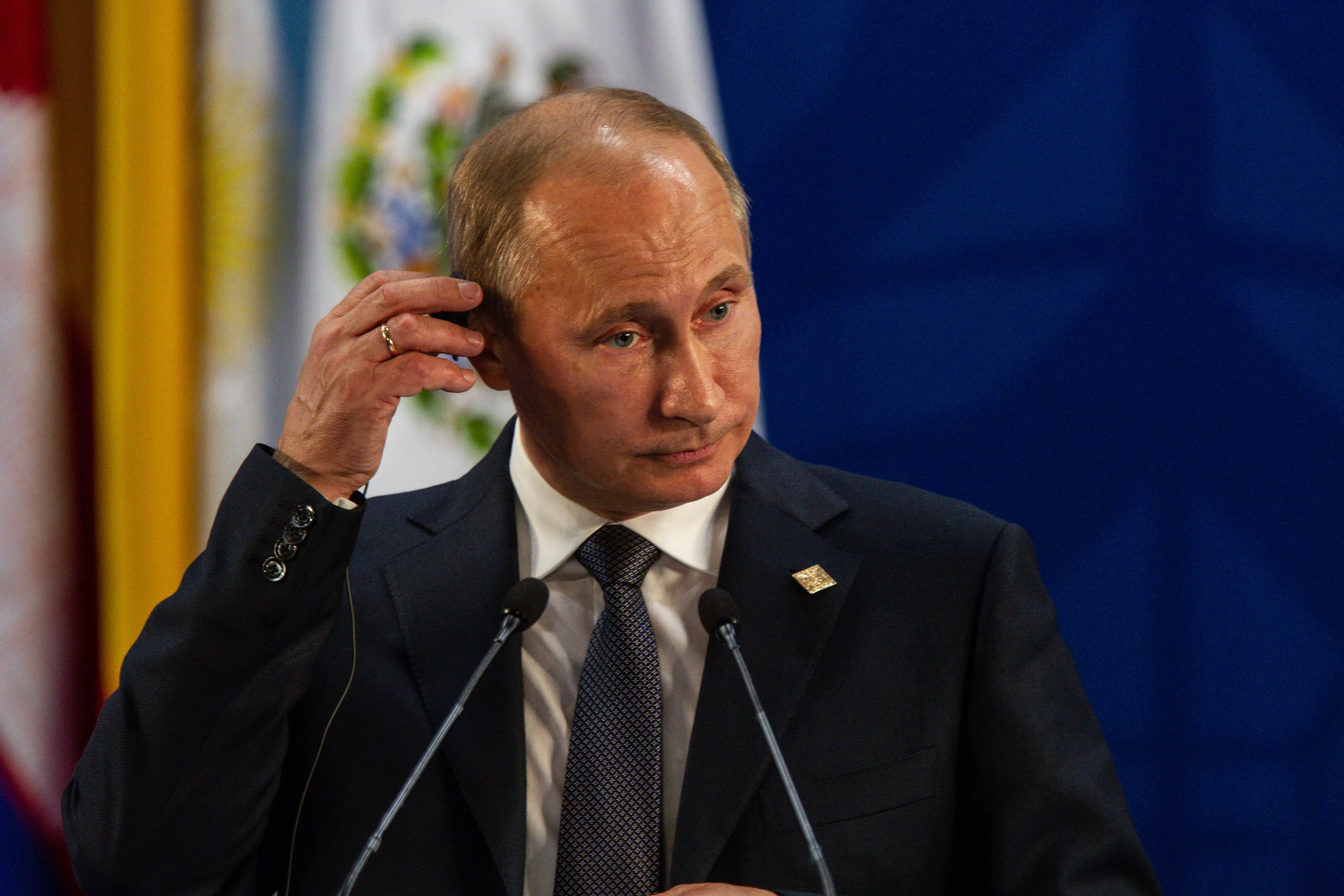 Vladimir Putin, îmbrăcat într-un costum negru, își duce mâna la ureche